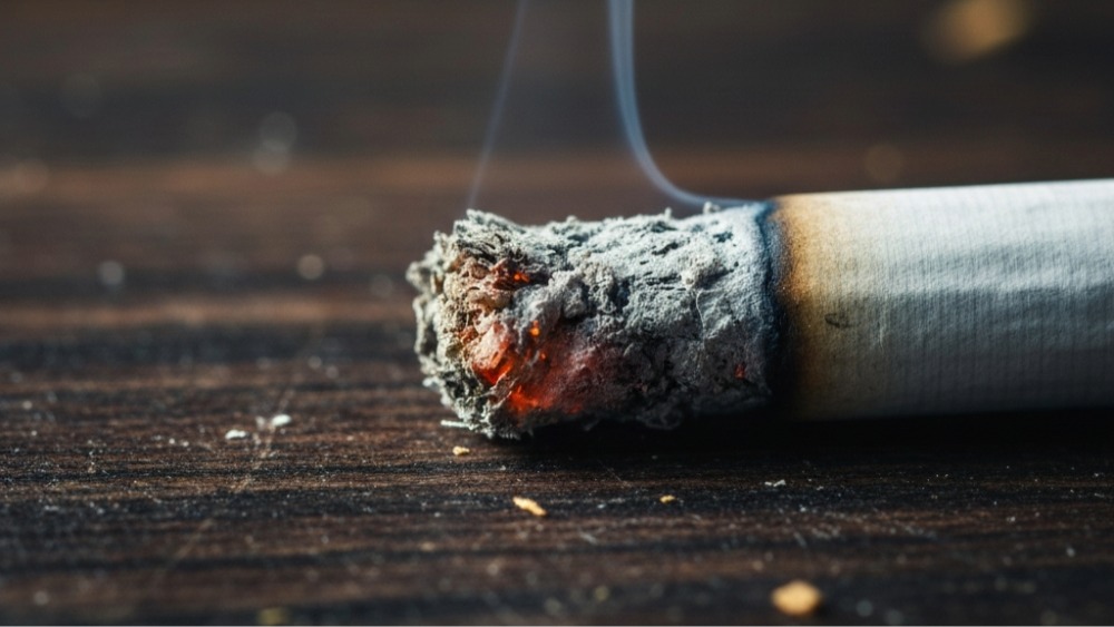 Close-up of burning cigarette showing glowing ember, gray ash accumulation and smoke demonstrating cigarette burn rate factors